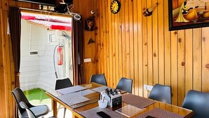 Ein Holzinterieur mit einem Esstisch, Stühlen, einem Deckenventilator, einem Fernseher und einer Uhr.
