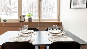 Una mesa de comedor dispuesta con platos, vasos y cubiertos, cerca de una ventana con vistas a árboles sin hojas.