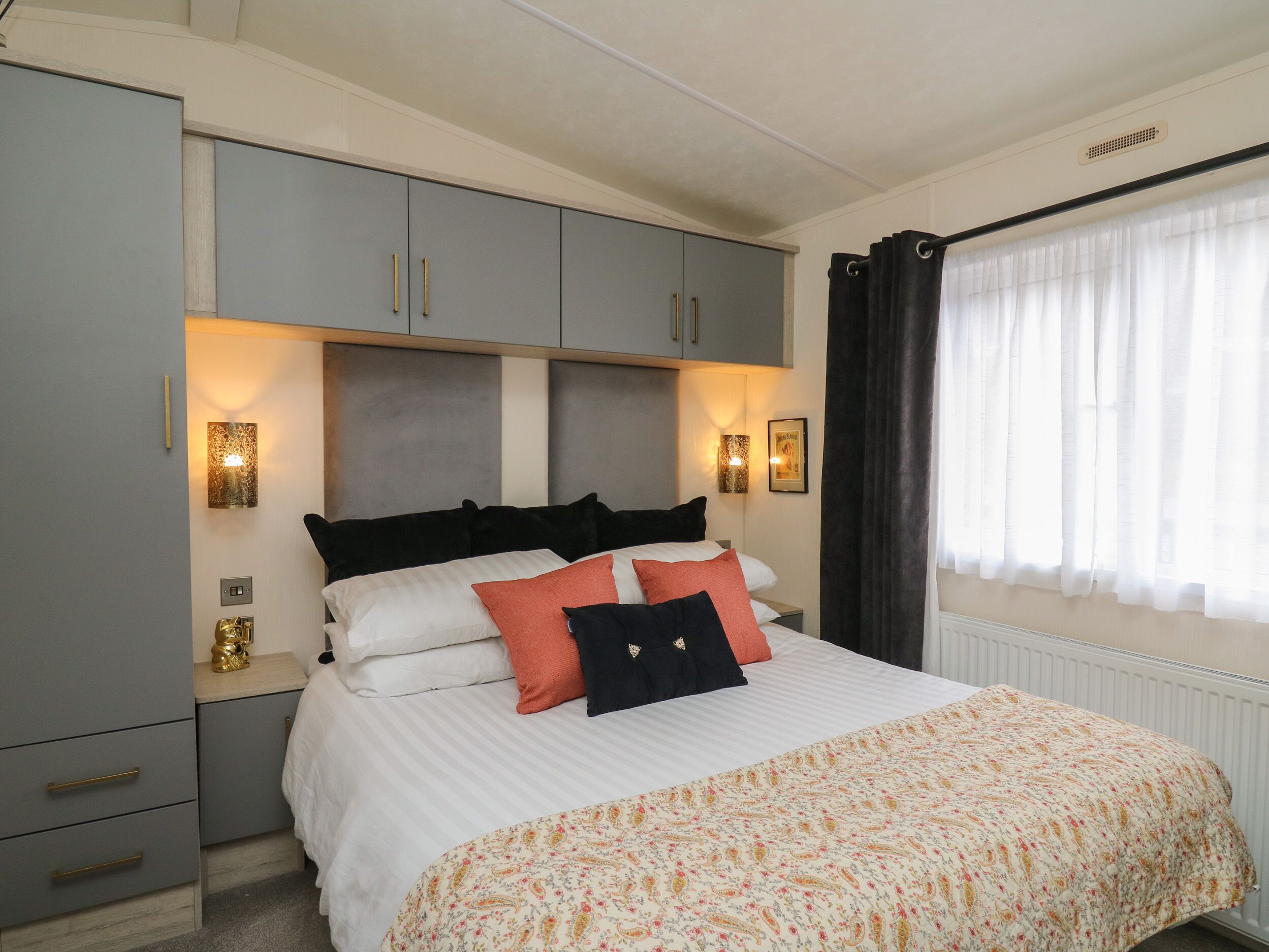 A bedroom with a bed, grey wardrobe, wall-mounted lights, and a window with curtains.