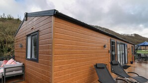 A wooden cabin with a deck, a lounge chair, and a small seating area. - The Hideout (New Quay)