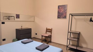 Un dormitorio con cama, una silla de madera, cómoda, espejo y estante en la pared.