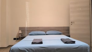 Habitación de hotel con cama, dos almohadas, mesita de noche con lámpara y una puerta.