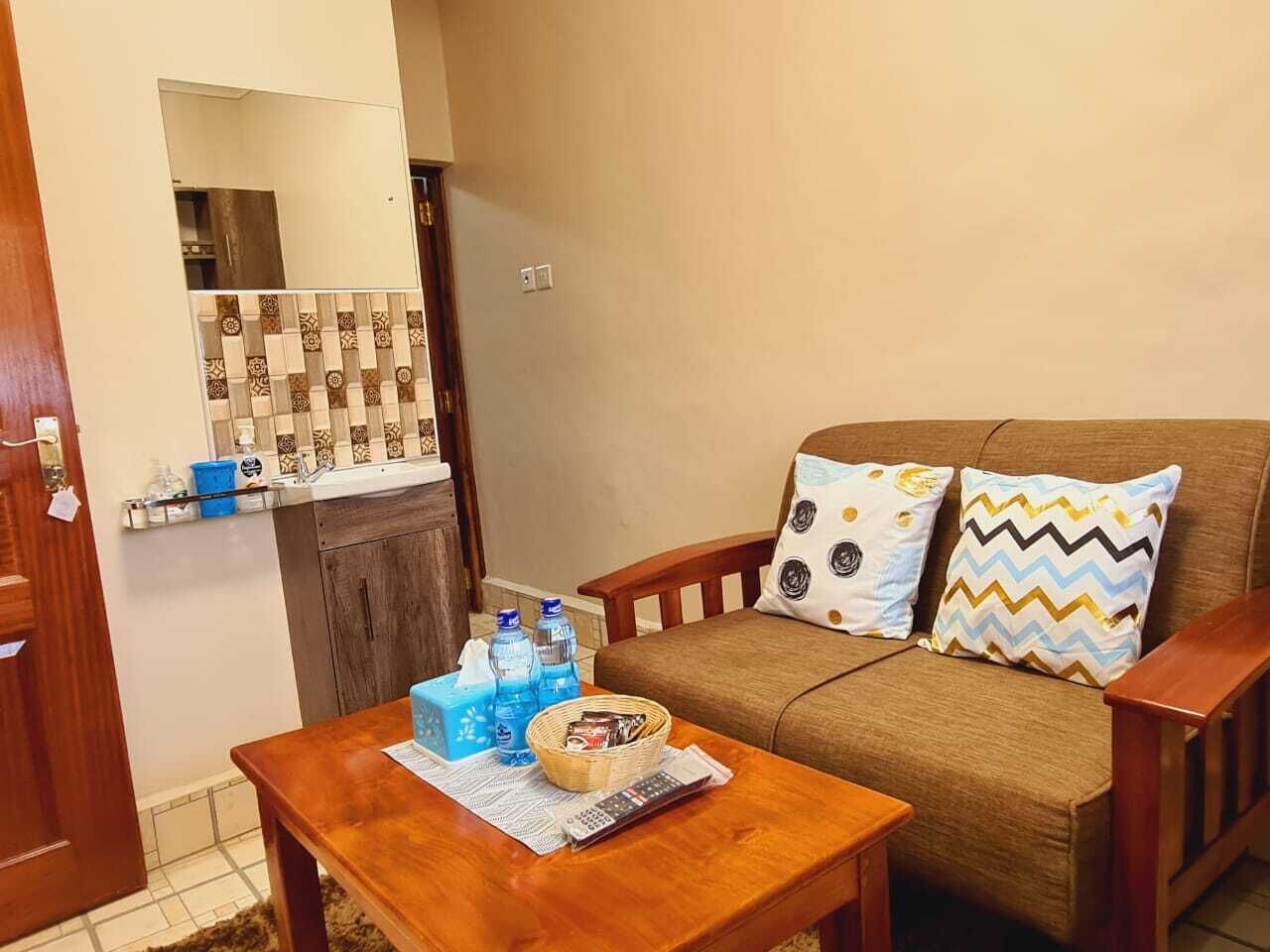 Cómoda sala de estar con un sofá marrón, dos cojines estampados, una mesa de centro de madera con una caja de pañuelos, agua embotellada y una cesta.