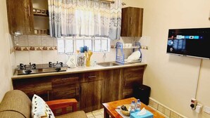 A compact living space with a kitchenette, a sofa, a wooden table, and a flat-screen TV mounted on the wall. - Lux Suites Geanna Suites Nanyuki (Nanyuki)