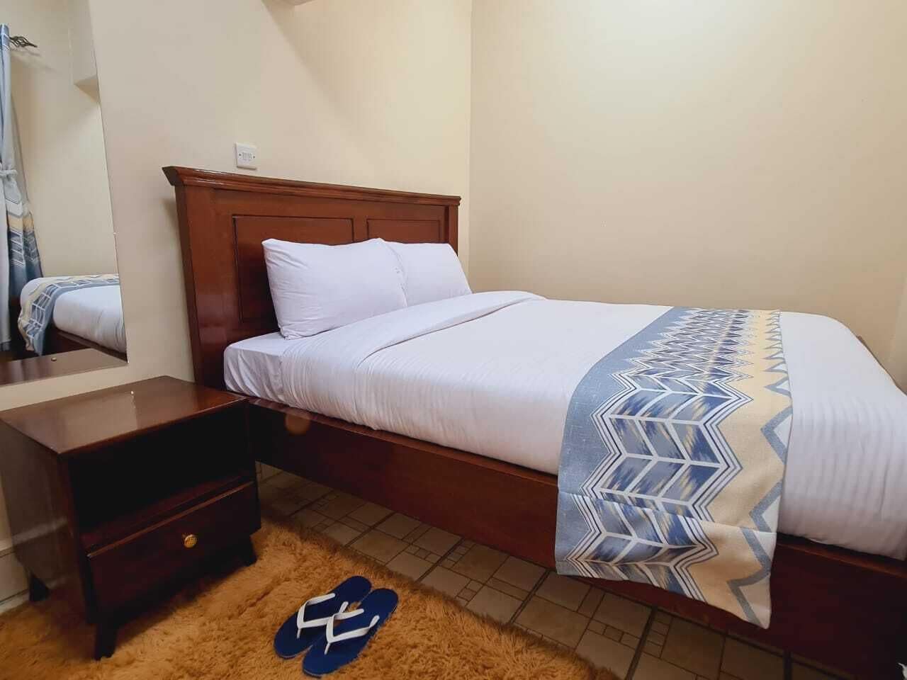 A single bed with a wooden headboard, a bedside table, and a patterned throw blanket.