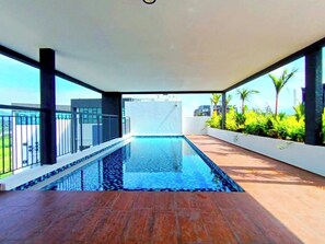 Piscina interior moderna con suelo de baldosas, rodeada por un balcón con barandilla y plantas.
