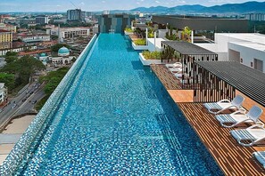 Piscina infinita en la azotea con vistas a la ciudad, sillones de descanso y una terraza de madera.