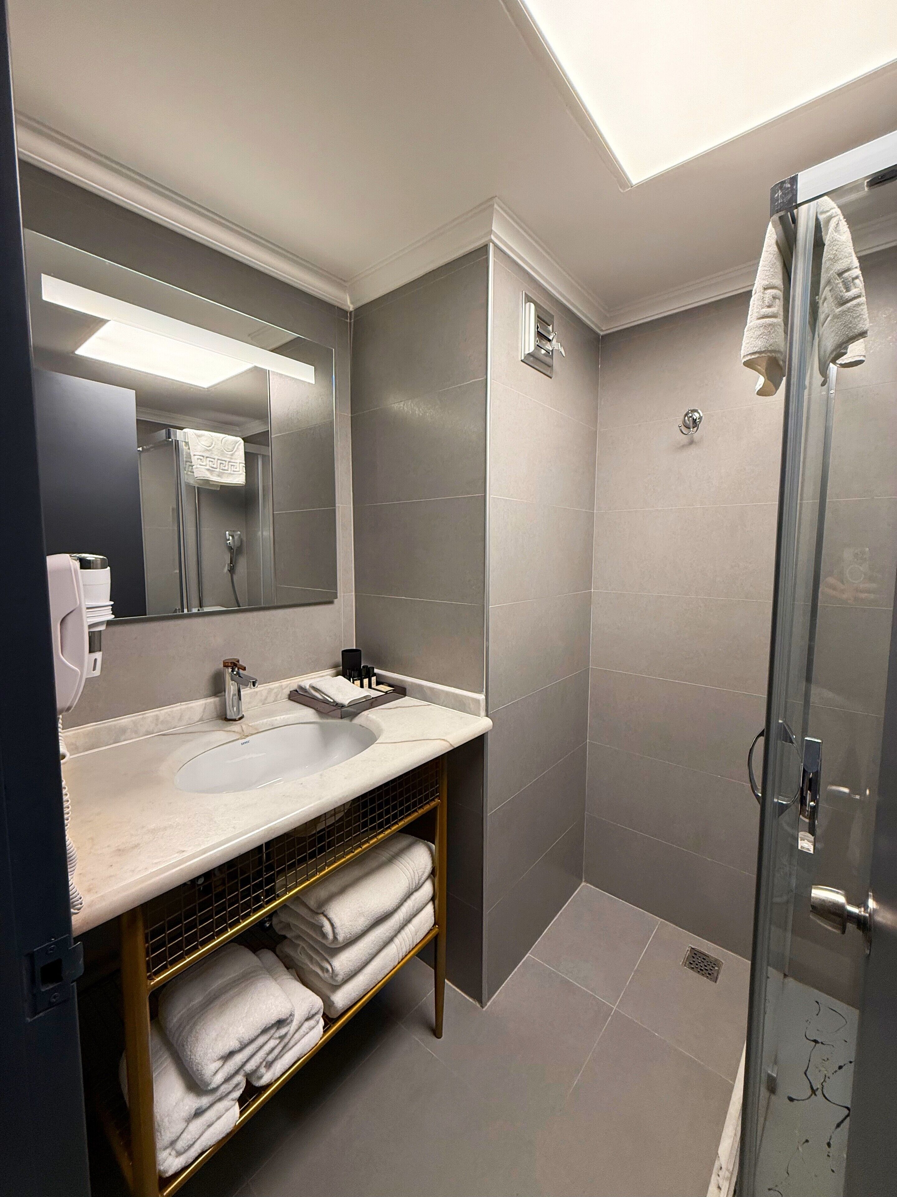 Un bany modern amb un mirall gran, un lavabo i una dutxa amb portes de vidre.