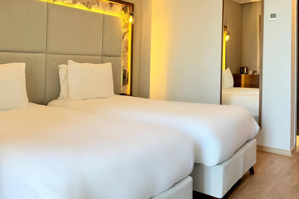 Een hotelkamer met twee bedden, een grote spiegel en een houten vloer.
