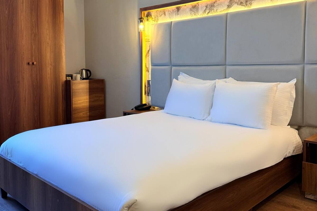 Een groot bed met houten frame, hoofdbord met lamp en nachtkastje met een lamp.