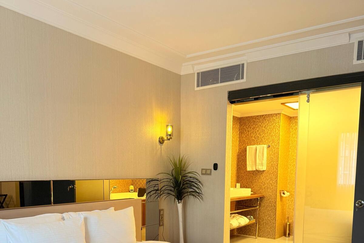 Een hotelkamer met een groot bed, een nachtkastje, een wandlamp en een schuifdeur naar een badkamer.