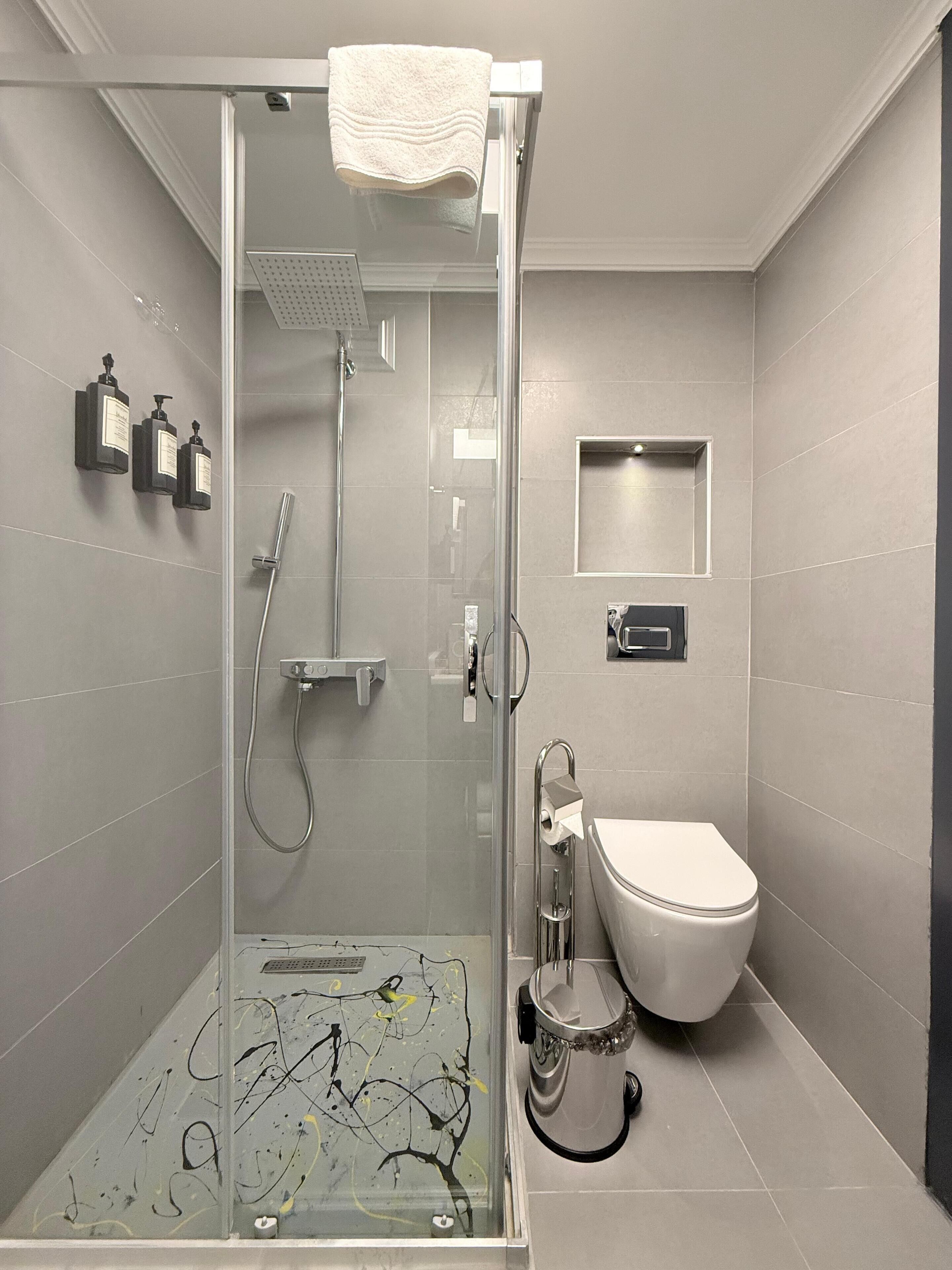 Un baño moderno con ducha de vidrio, inodoro y un espejo pequeño.