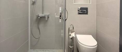 Un baño moderno con ducha de vidrio, inodoro y un espejo pequeño.