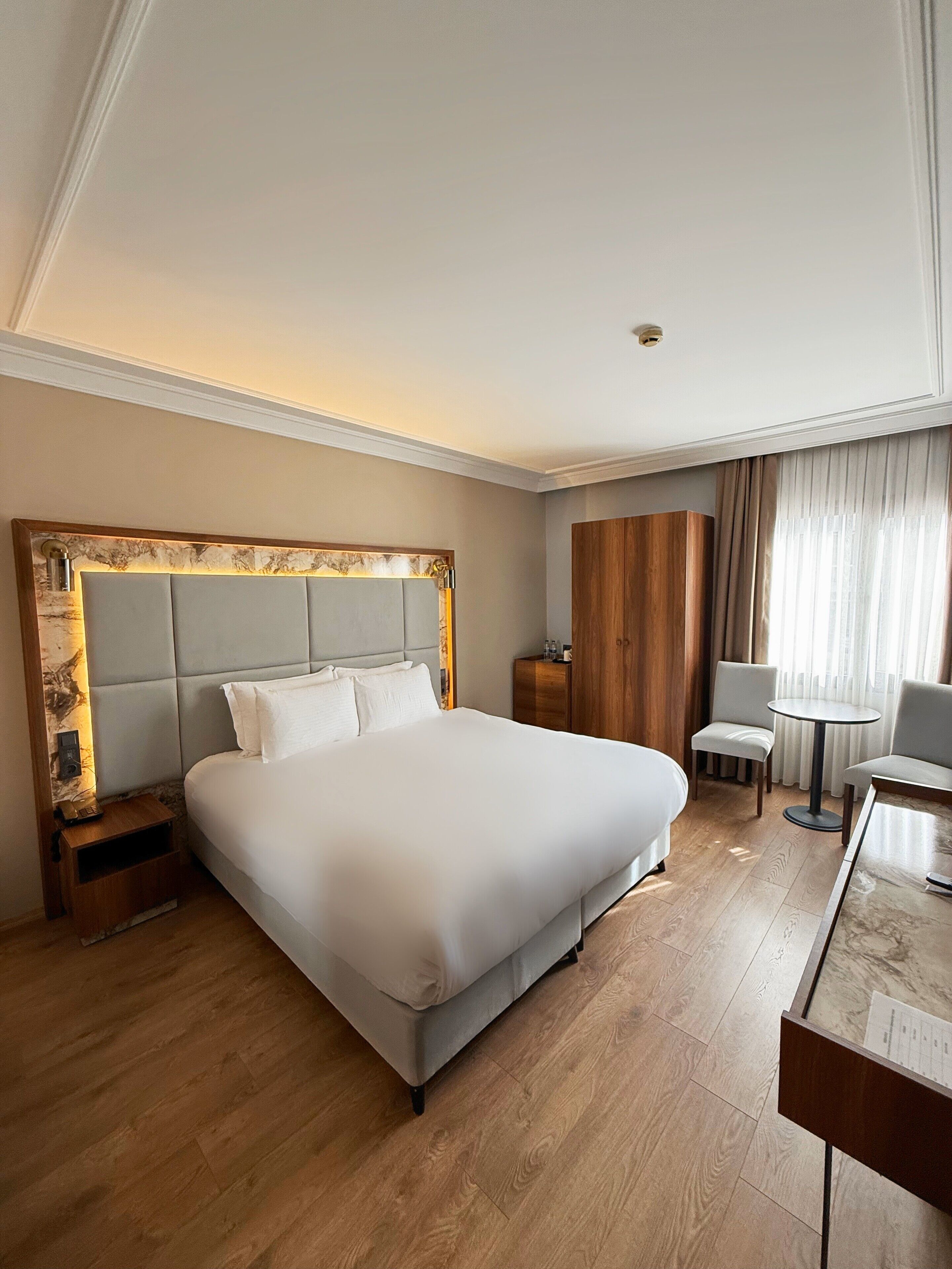 Una camera d'hotel con un letto grande, un armadio in legno, un tavolino e una sedia.