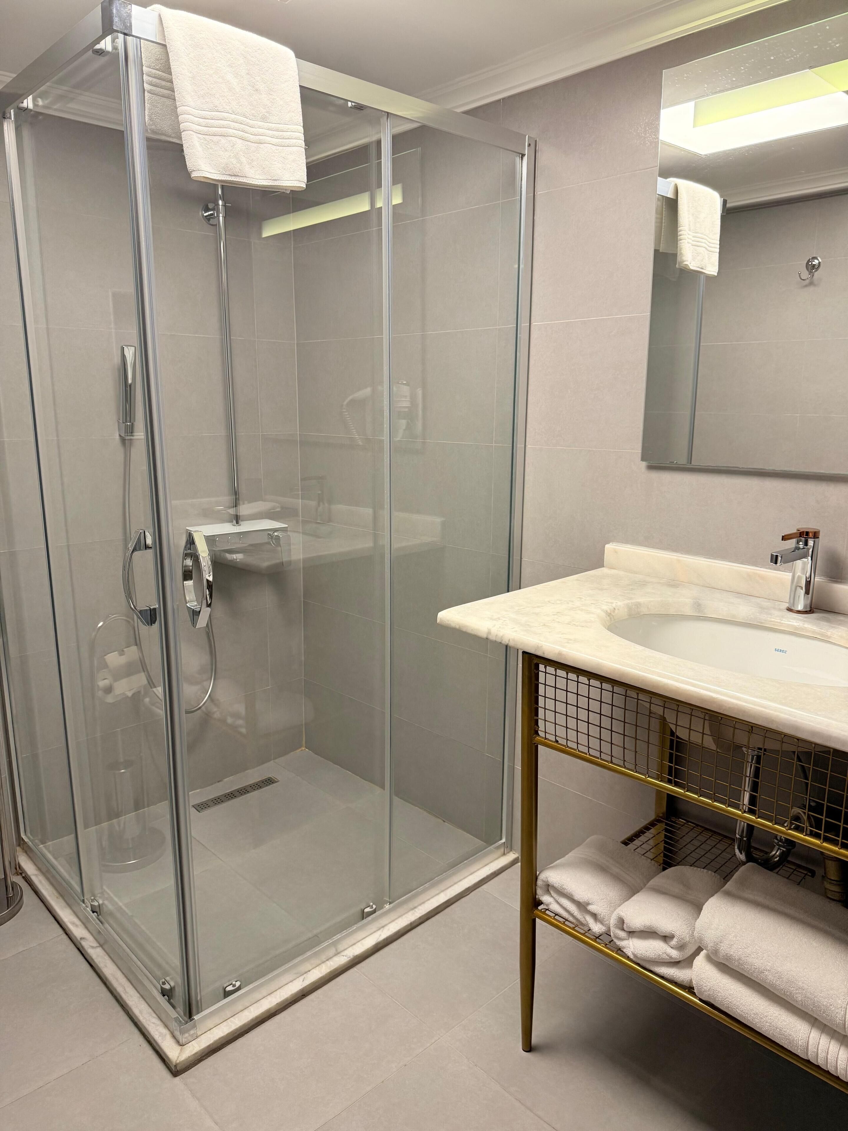 Une salle de bain moderne avec une douche à parois de verre, un lavabo doté d’un plan de travail en marbre et un miroir au-dessus du lavabo.