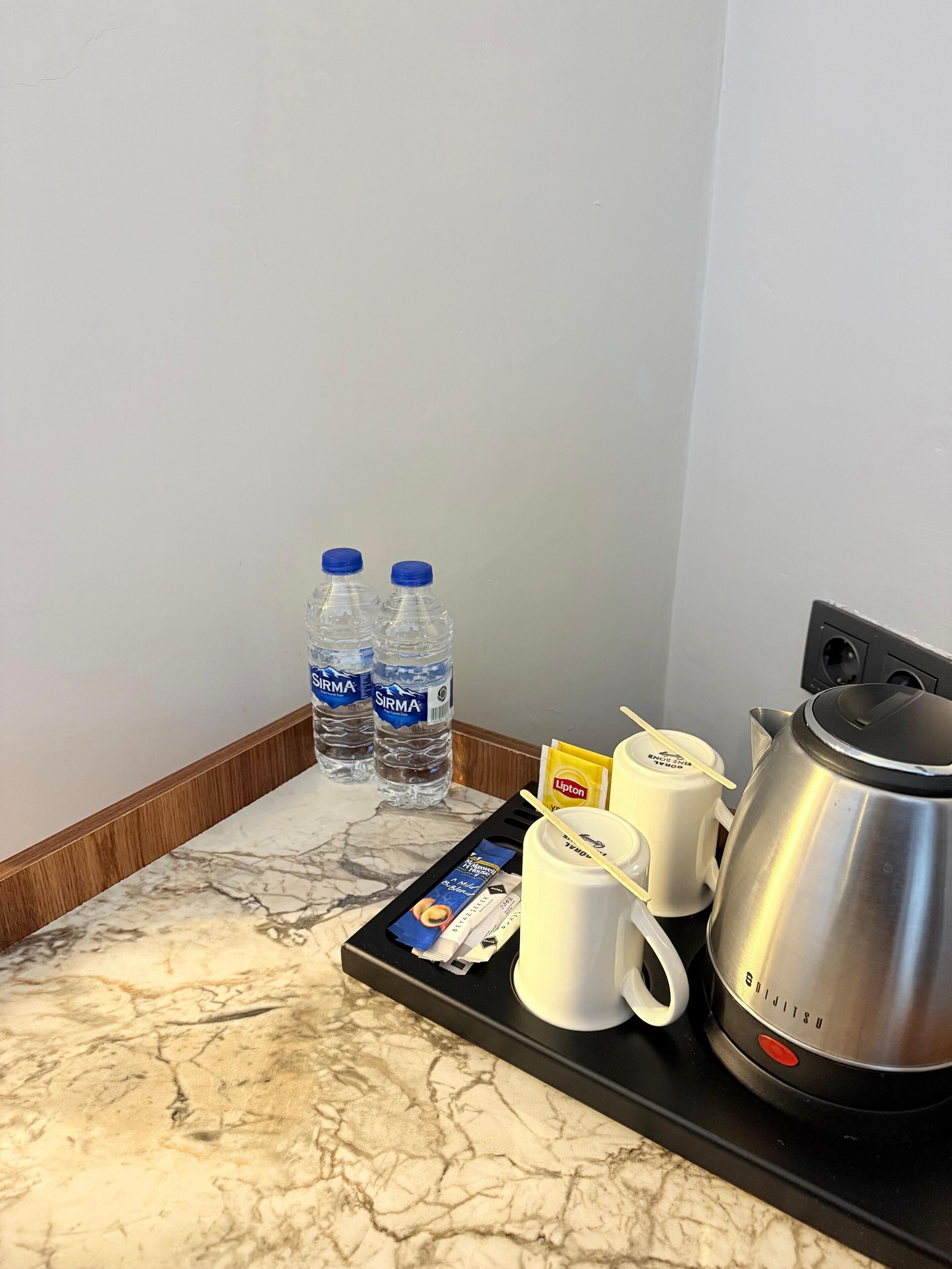A marble countertop with a tray holding a coffee maker, two white mugs, a packet of Lipton tea, and two water bottles.