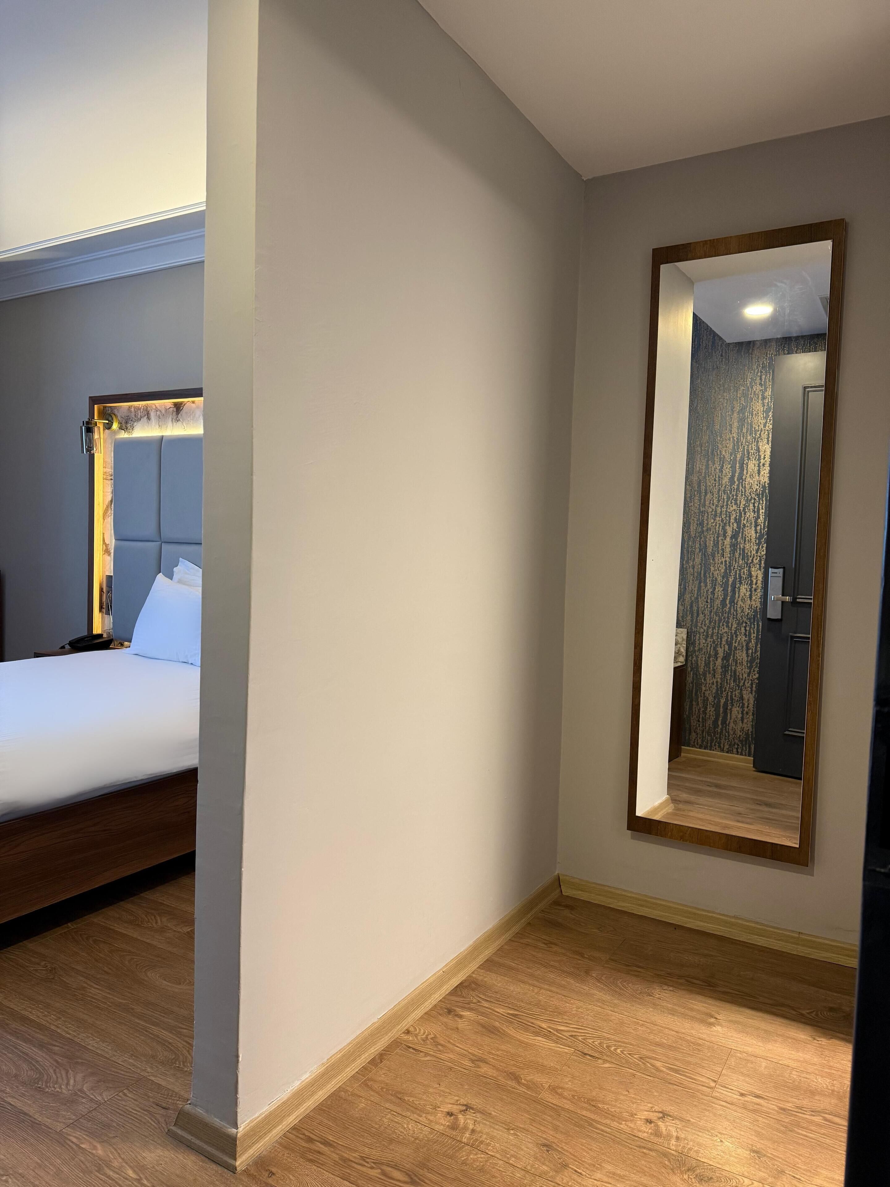 A hotel room with a large bed, a wooden floor, a mirror, and a door.