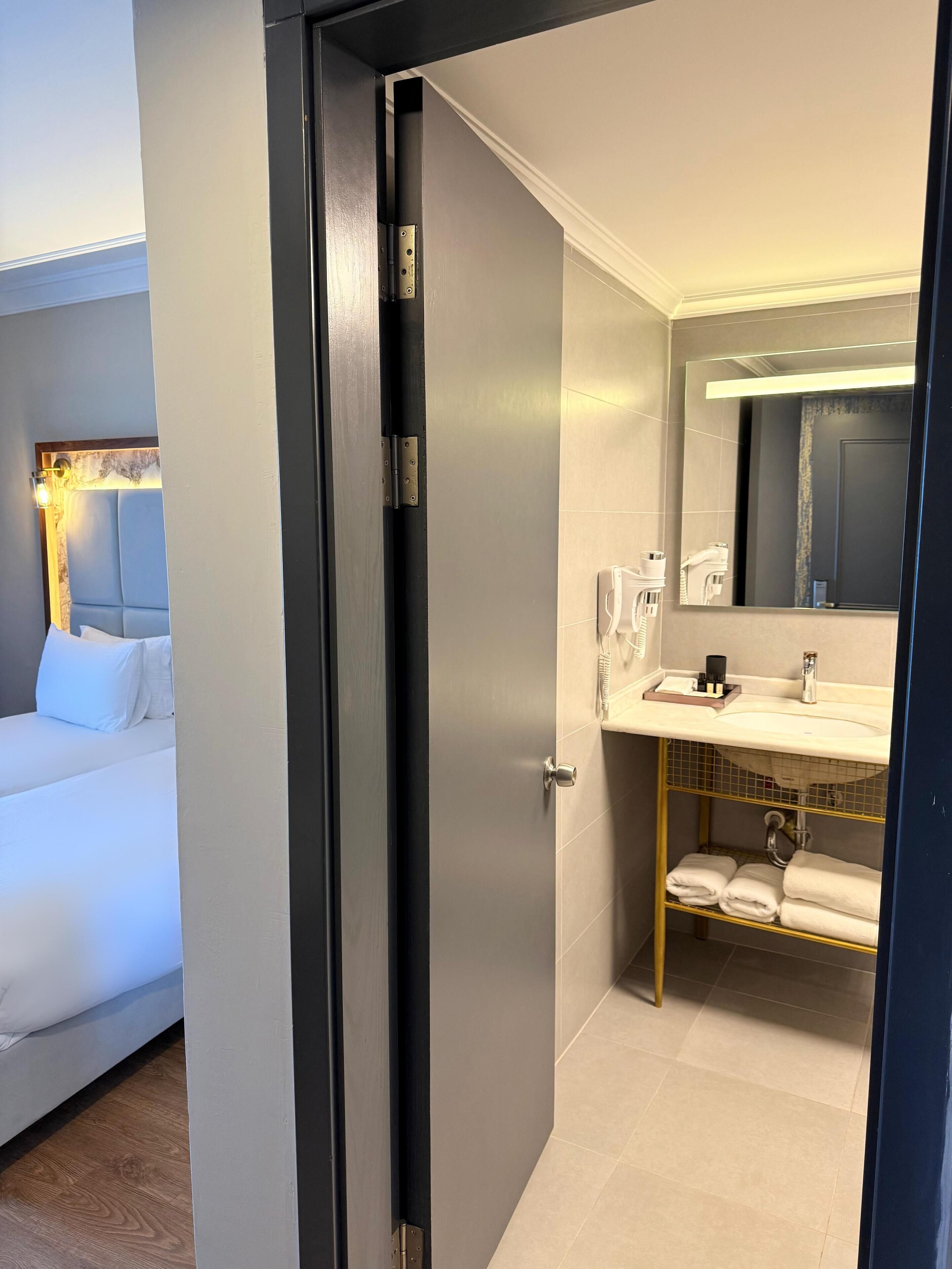 A hotel room with a bed, a bathroom with a sink and mirror, and a door leading to another room.