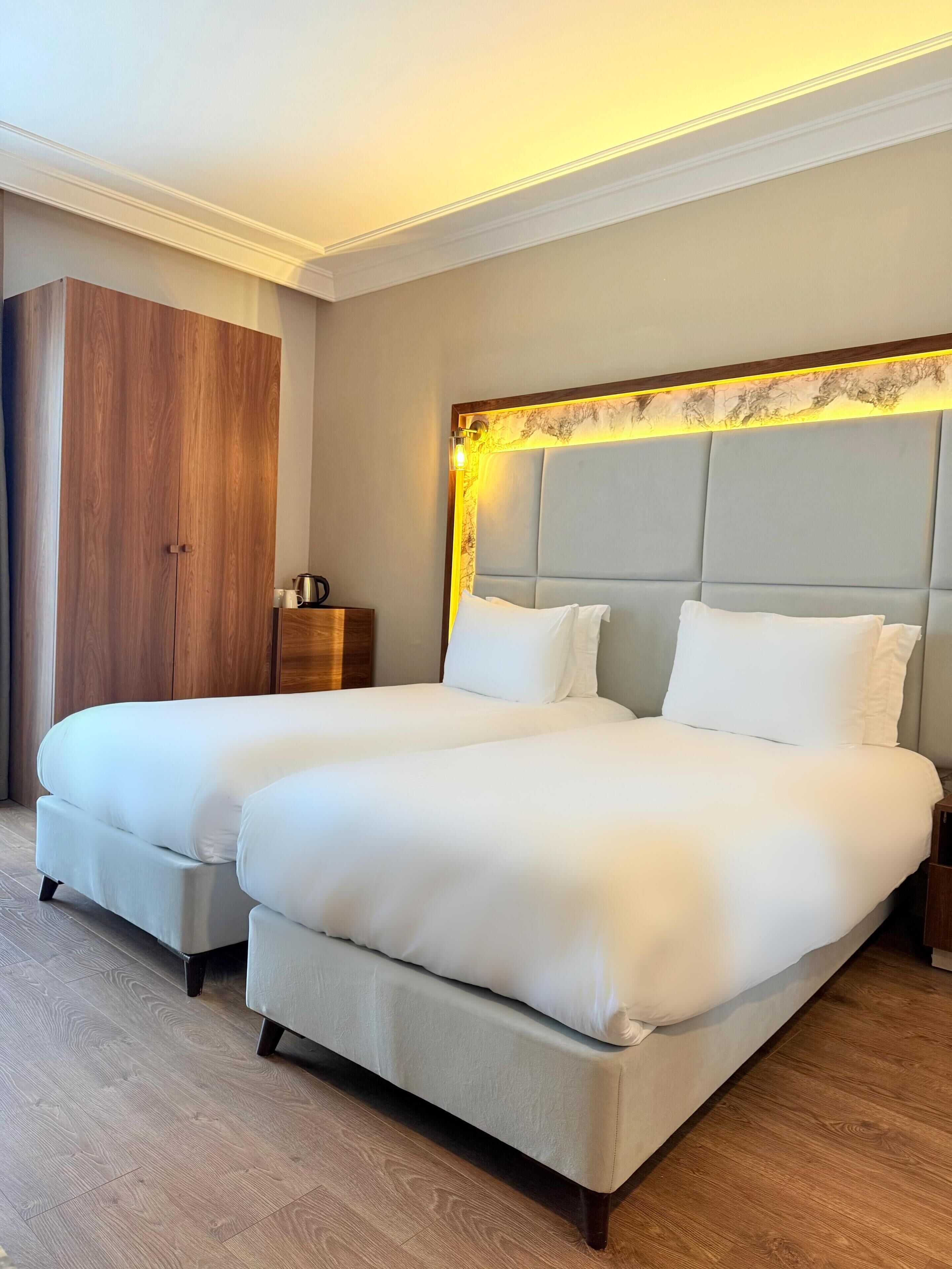 Een tweepersoonsbed met hoofdbord, een houten garderobe en een nachtkastje met lamp.