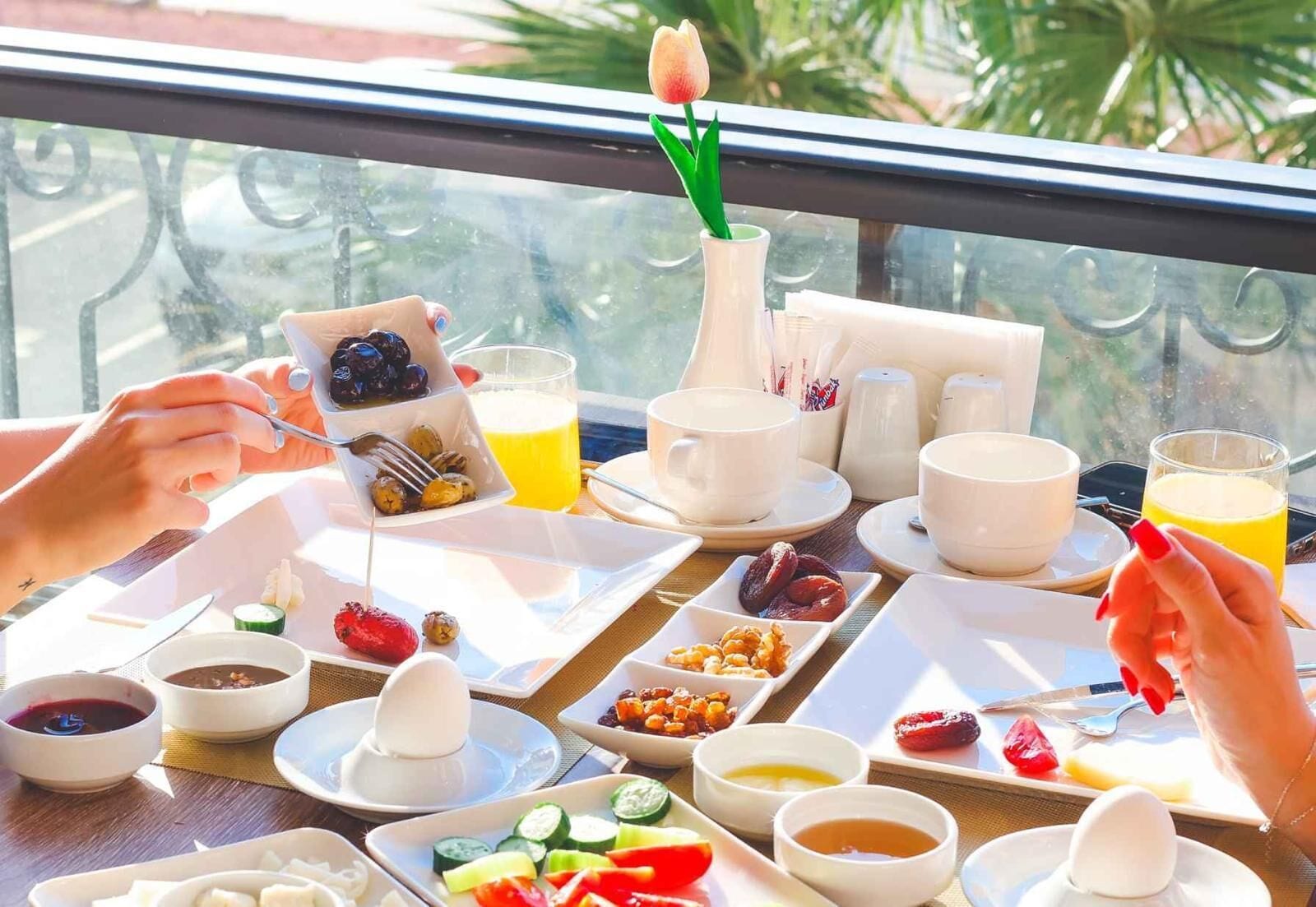 Une table de petit-déjeuner avec différents plats, une tulipe et une vue sur la fenêtre.