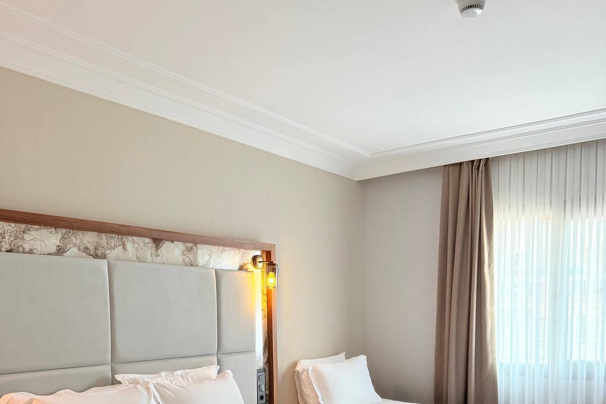 Een hotelkamer met twee bedden, een hoofdeinde, een nachtkastje, een lamp en een raam met gordijnen.