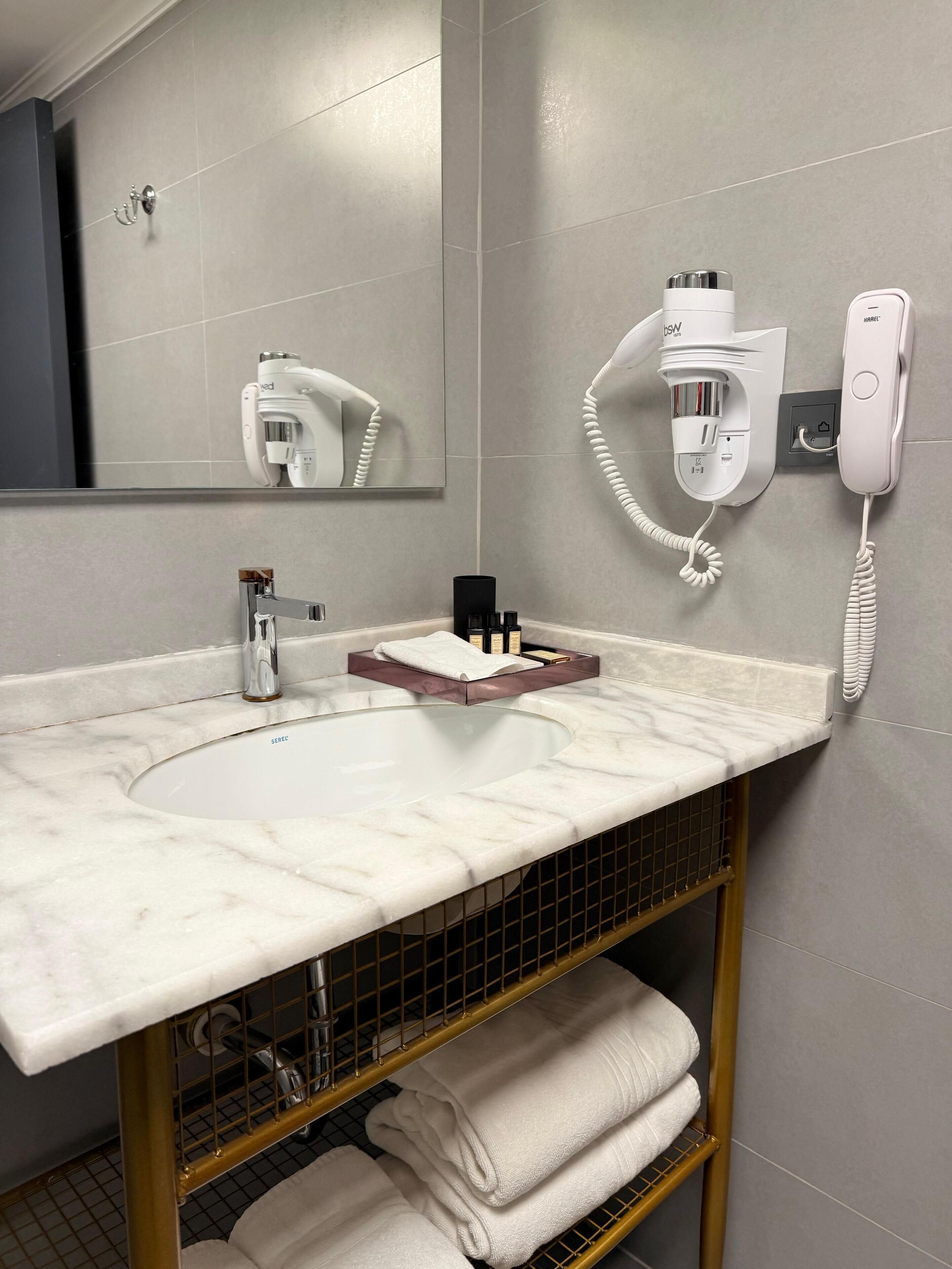 Uma casa de banho moderna com lavatório de mármore, secador de cabelo, telefone e um porta-toalhas.