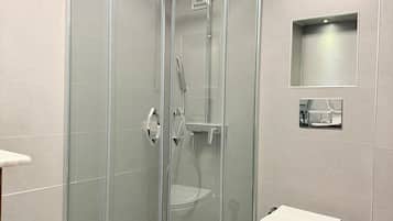 Een moderne badkamer met een douche met glazen wand, een wit toilet en een klein plankje met een spiegel.