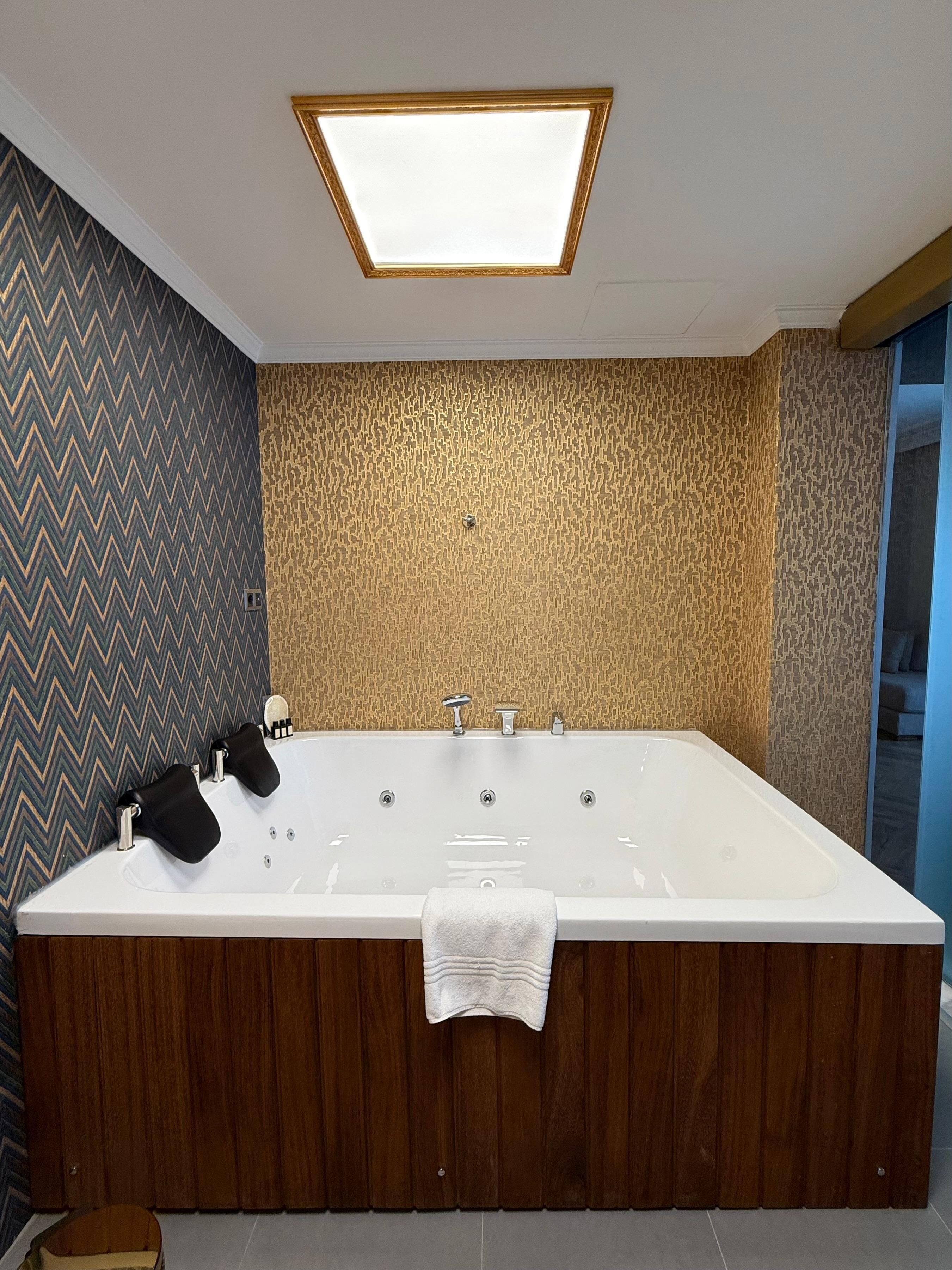 A modern bathroom with a freestanding bathtub, a wooden vanity, and a patterned wall.