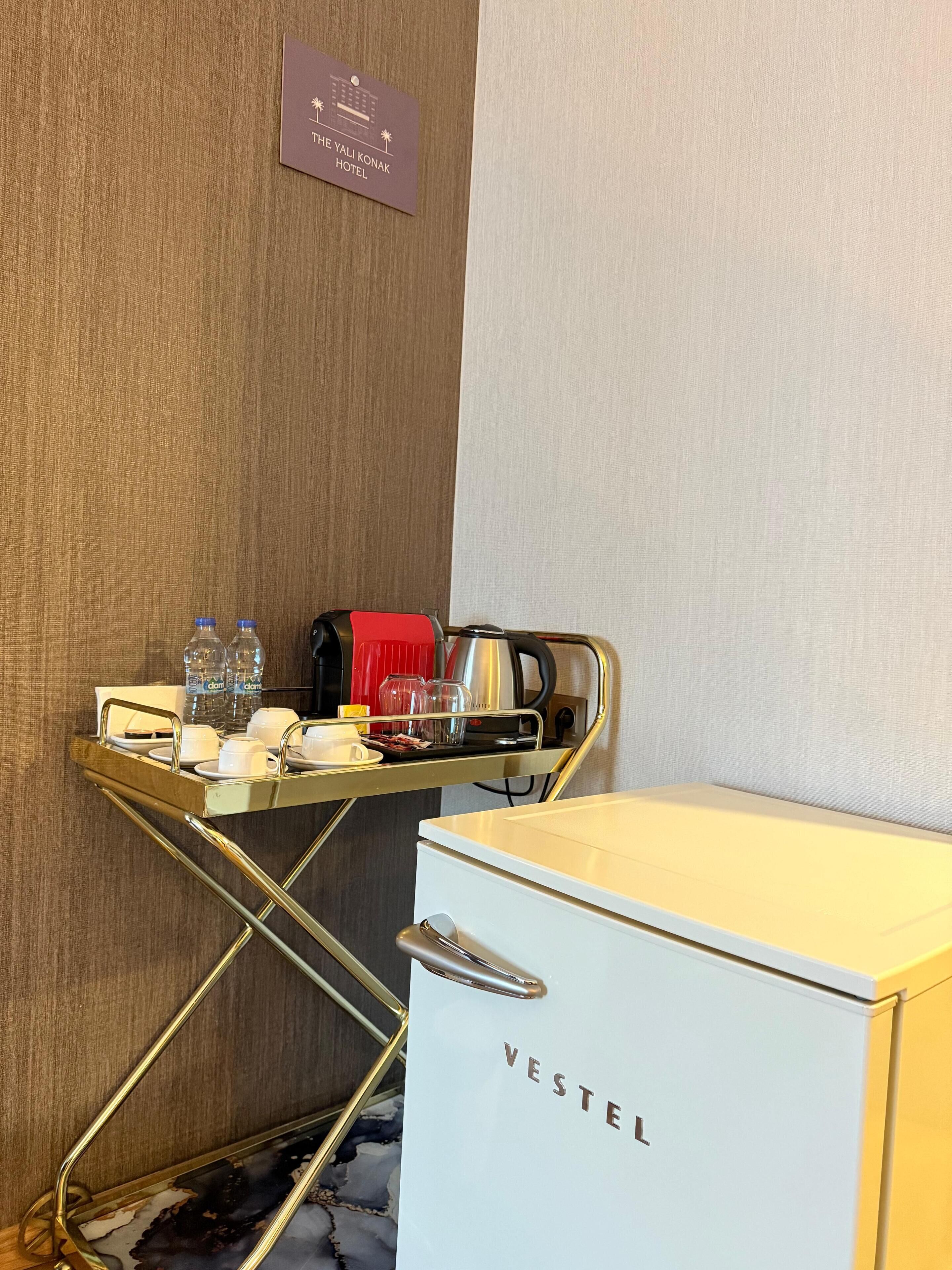A hotel room with a minibar, a water dispenser, a coffee maker, and a white minibar branded "VESTEL".