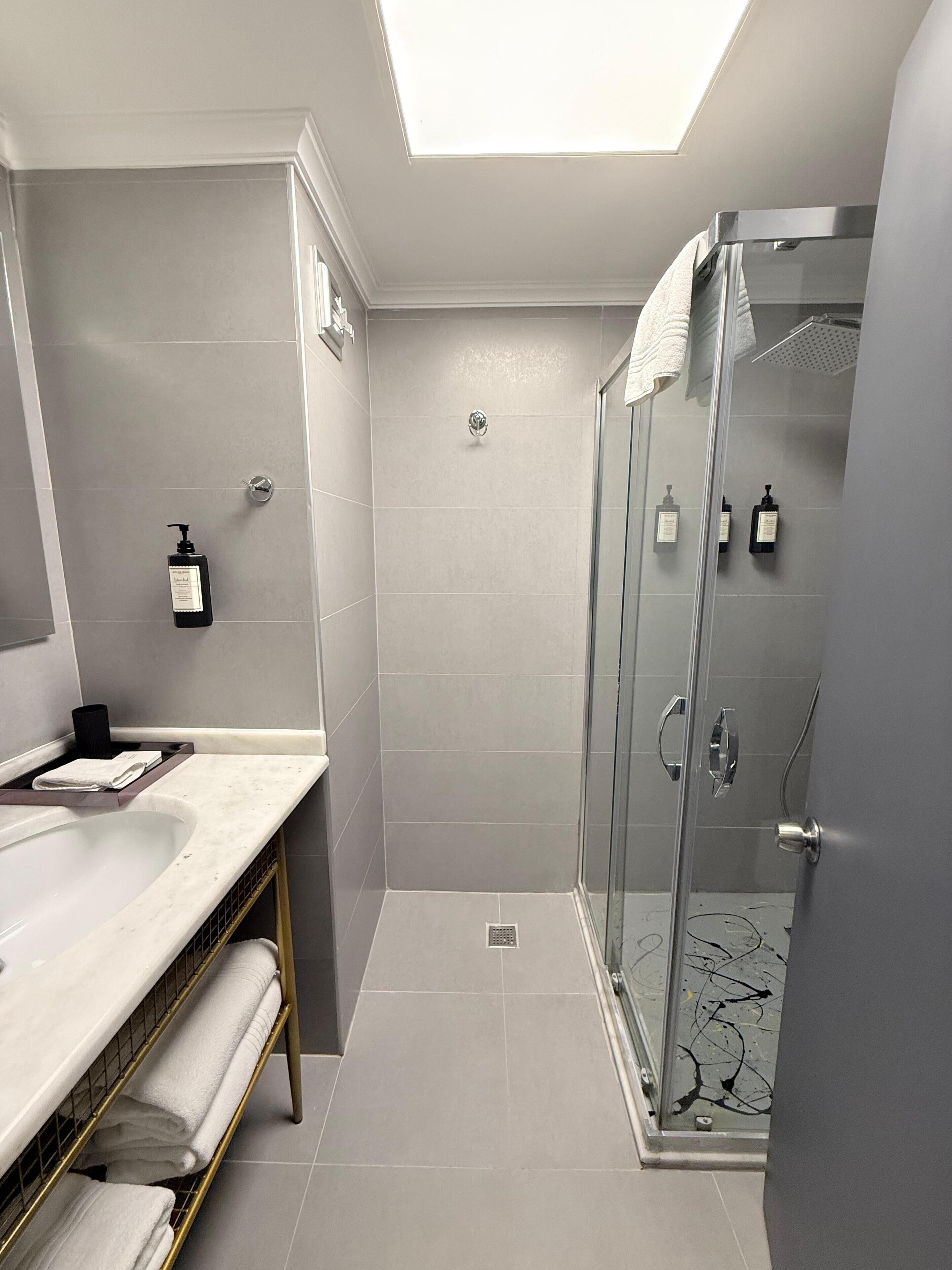 A modern bathroom with a glass-enclosed shower, a vanity with a marble countertop, and neatly folded towels on a rack.