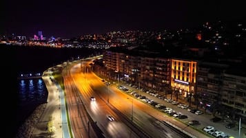 Un paisaje urbano nocturno con una autopista bien iluminada, un estacionamiento y un edificio con señalización luminosa.