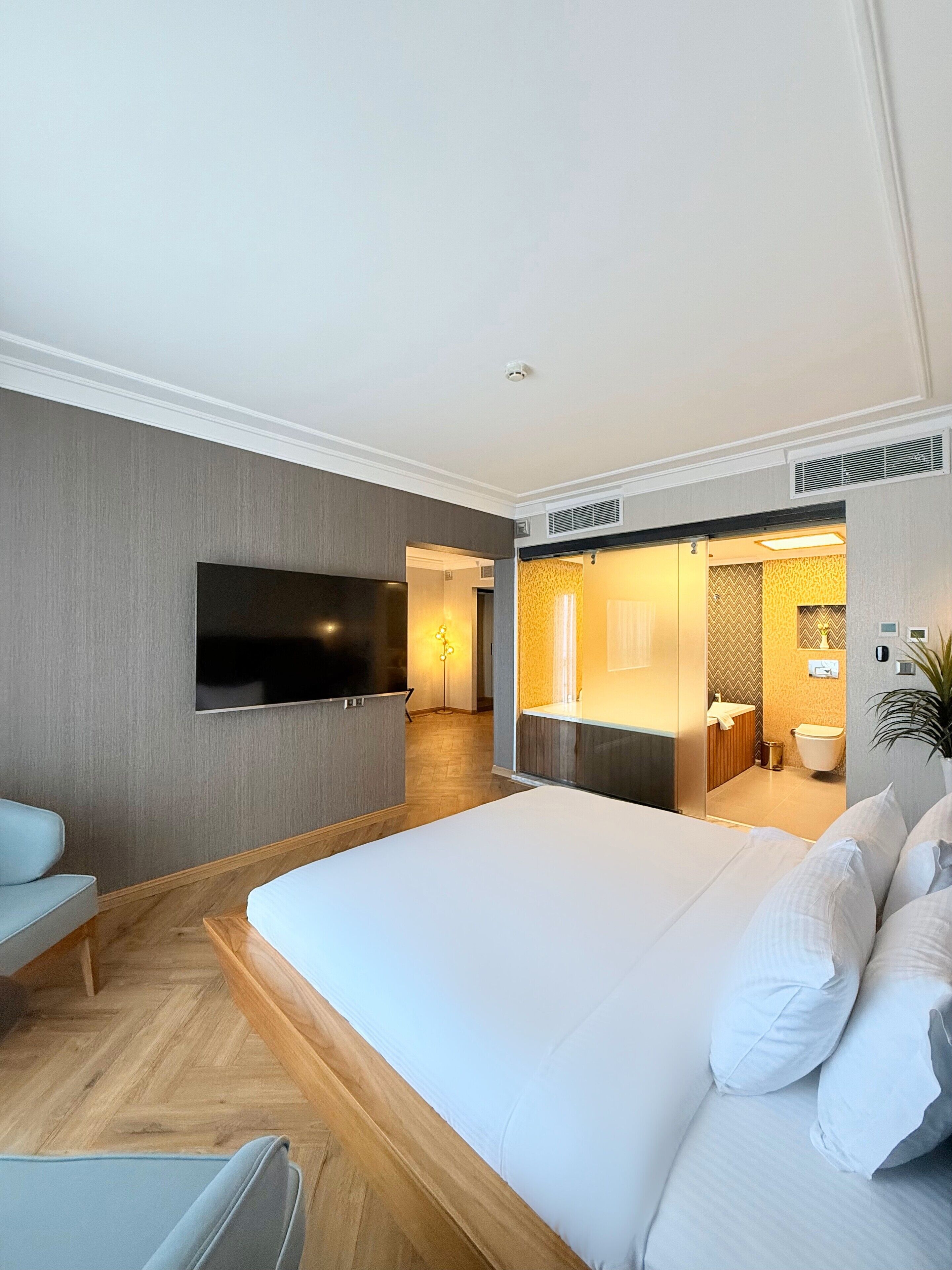 A modern hotel room with a large bed, a flat-screen TV, a sofa, and a bathroom with a shower and toilet.