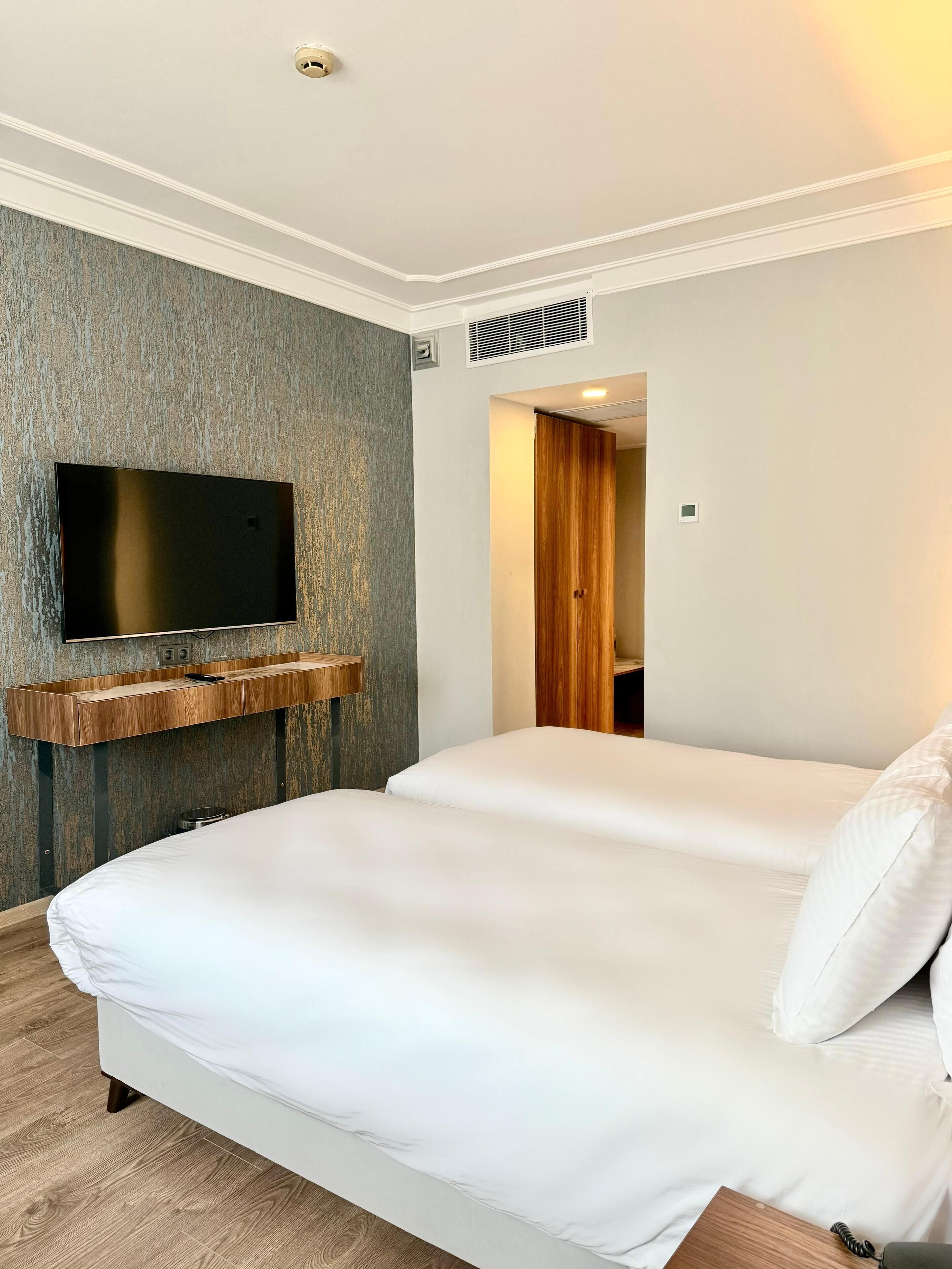 A hotel room with a large bed, a mounted TV, and a wooden shelf.