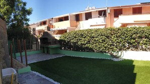 A courtyard with artificial grass, a stone pathway, a stone barbecue area, and a hedge. - Summer vacations in Villasimius in a beautiful villa with garden (Sardegna)