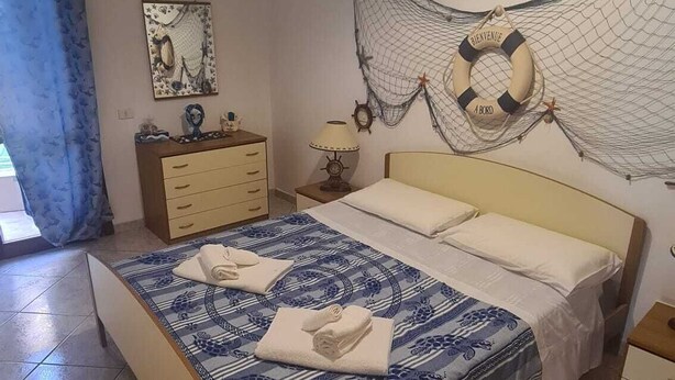 A bedroom with a bed, a dresser, a nightstand, a lamp, and a wall decoration. - Summer vacations in Villasimius in a beautiful villa with garden (Sardegna)