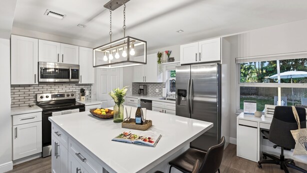 A modern kitchen with white cabinetry, stainless steel appliances, and a large island with seating.