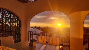 Ein Balkon mit Tisch und Stühlen, einem Blumentopf und Blick auf den Sonnenuntergang.