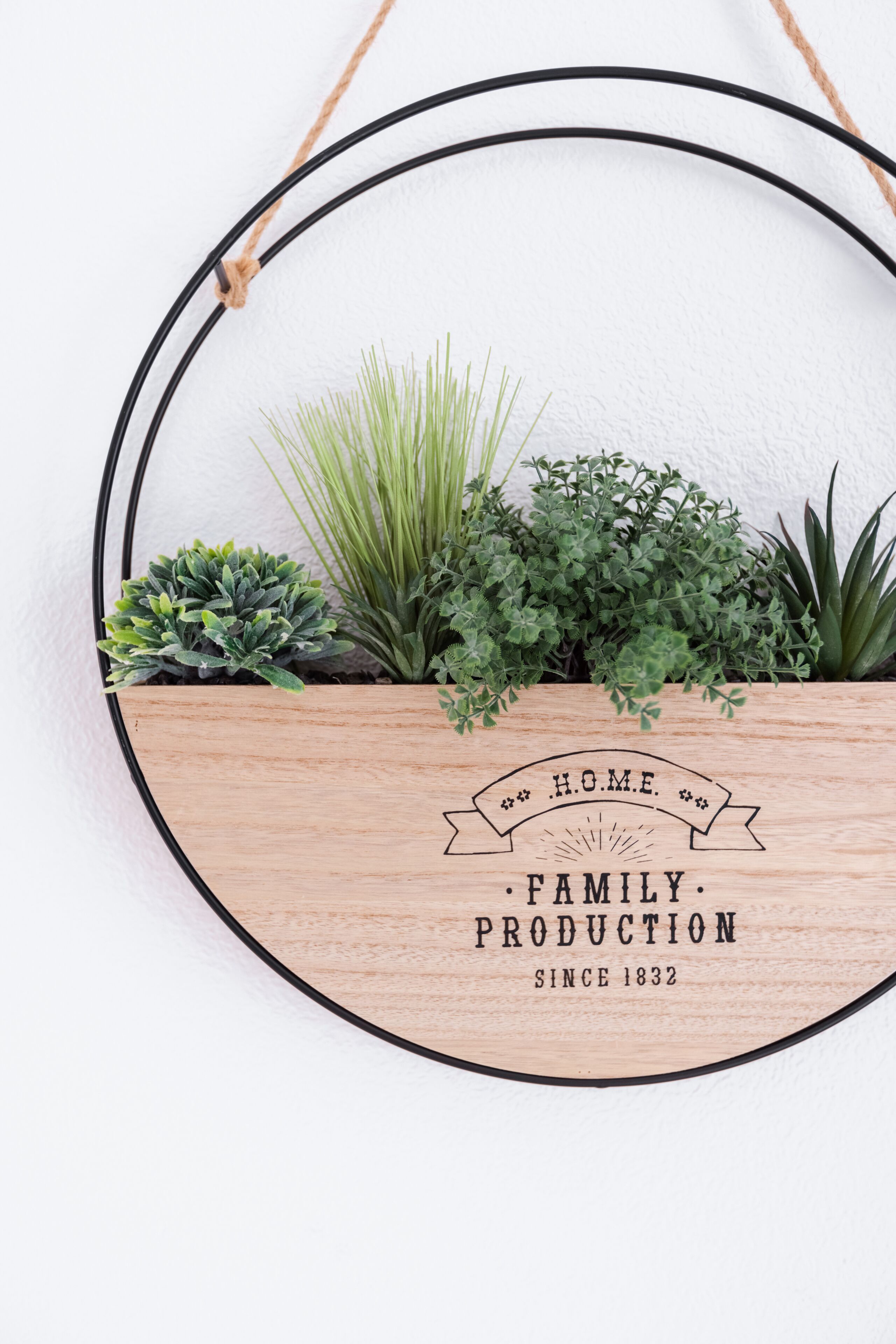 A wooden planter with a black circular frame, containing various green plants, and a banner with text.