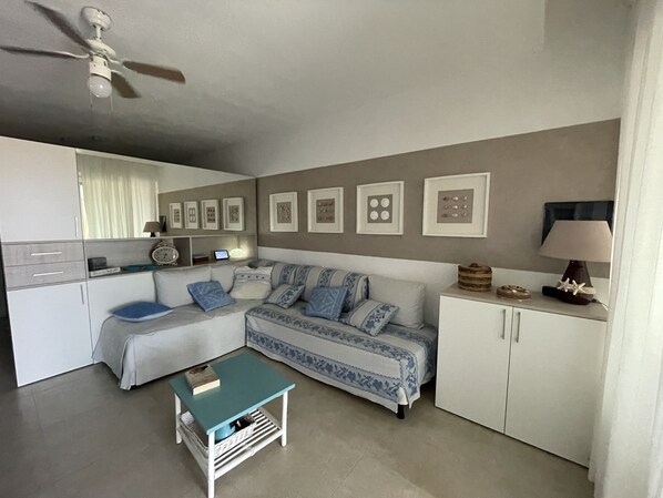 A compact living space with a sofa, a small coffee table, a cabinet, and a ceiling fan.