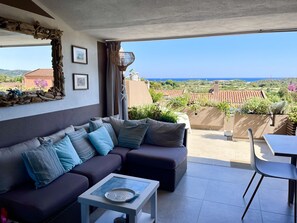 A balcony with a sofa, a table, and a view of the sea and surrounding buildings.