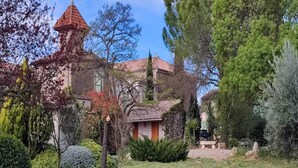 A traditional building with a red-tiled roof, surrounded by lush greenery and a well-maintained garden.