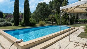 A rectangular swimming pool with a tiled edge, surrounded by a tiled deck and a covered area with metal railings.