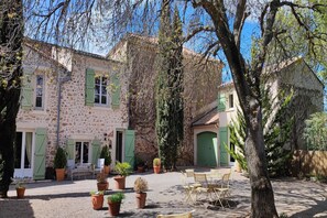 A stone building with green shutters, a courtyard with potted plants, and outdoor seating. - Beautiful domaine with private pool and park (Cazouls-les-Béziers)