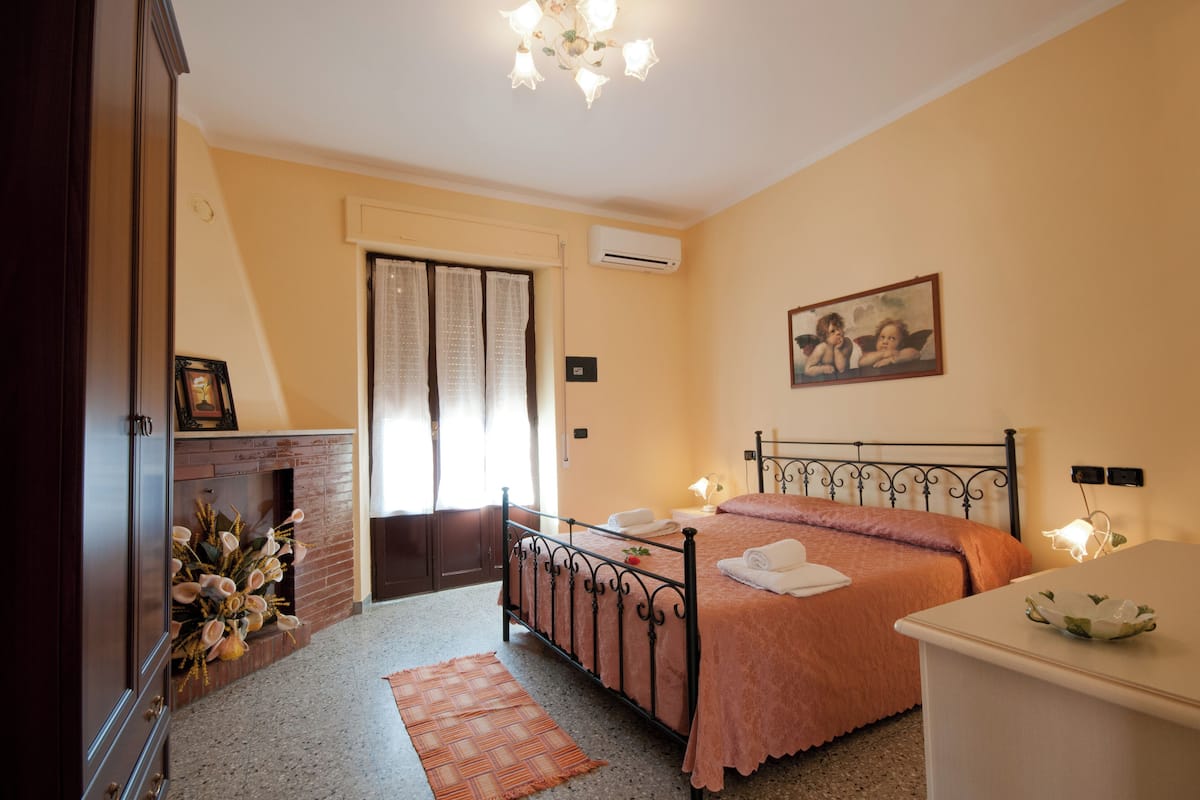Ein Schlafzimmer mit einem Bett, einem Kamin, einem Bild an der Wand und einem Nachttisch.