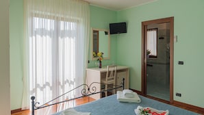 A bedroom with a bed, a desk, a chair, a TV mounted on the wall, and a bathroom door.