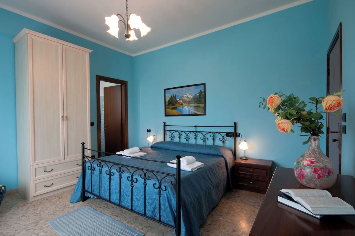 Ein Schlafzimmer mit einem Bett, einem Nachttisch, einer Kommode, einer Vase mit Blumen und einem Bild an der Wand.
