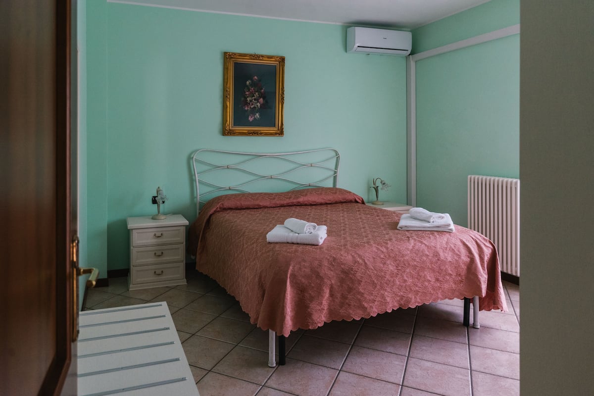 Ein Schlafzimmer mit Bett, Nachttisch, Kommode, einem gerahmten Bild an der Wand und einer Klimaanlage.