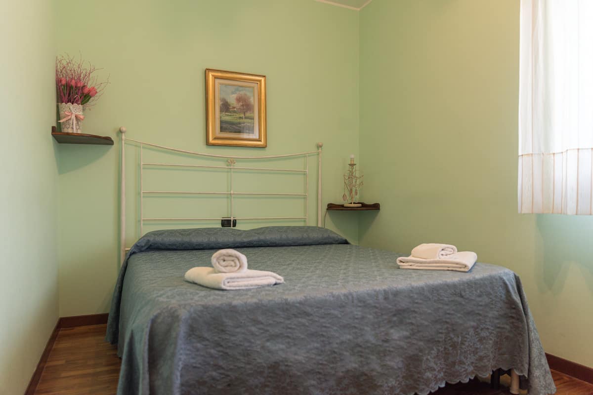 Ein Schlafzimmer mit einem Bett, Kissen, einem gerahmten Bild und einer Vase mit Blumen.