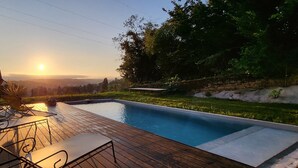 Une piscine avec une terrasse en bois, des chaises longues et une vue sur le coucher de soleil.