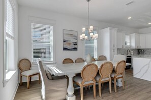 A modern kitchen with white cabinets, a dining area with a white table and wicker chairs, and a hanging light fixture. - Brand New Beautiful Beach Home/Minutes to Beach/Community Pool/Large screened-in patio/Sleeps 14 (Santa Rosa Beach)